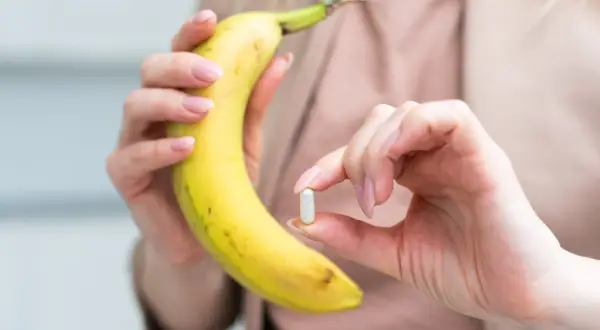 Dłoń trzymająca banana i tabletkę, przypominając o tym, na co jest potas i jak ważny jest dla organizmu.
