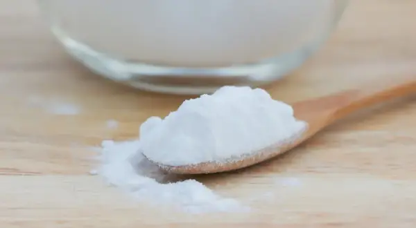 Łyżeczka sody oczyszczonej, znanej jako soda na zgagę, rozsypana na drewnianym blacie.